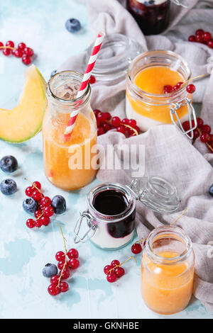 Variété de melon et de bleuets smoothie dans des bocaux en verre et bouteille avec le yogourt et petits fruits groseille rouge, servi sur le bleu clair textu Banque D'Images