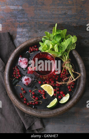 Ingrédients pour faire des cubes de glace limonade, baies de groseille rouge, de chaux, de citron et de menthe, servi avec un verre de jus sur le plateau d'argile wi Banque D'Images