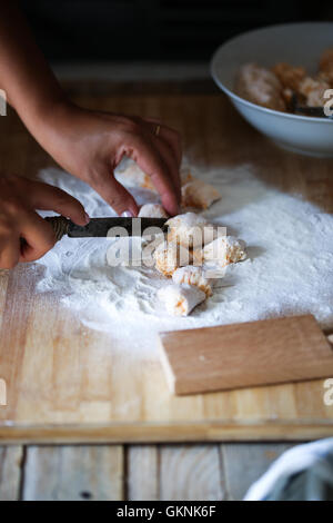 Une femme coupe la pâte pour préparer gnocchi maison Banque D'Images