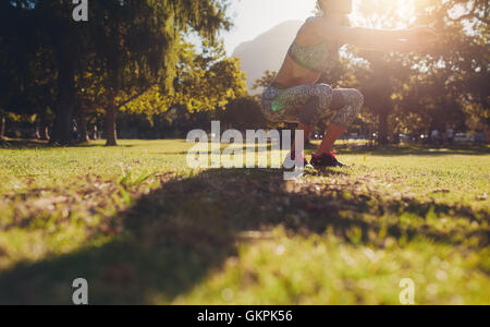 Prise de vue à angle bas d'une femme s'exerçant sur l'herbe au parc. fitness femme pratiquant l'exercice squat au parc un matin ensoleillé Banque D'Images