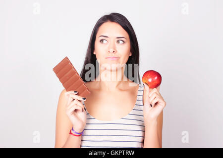 Young caucasian woman faire un choix entre le chocolat et d'Apple. Régime alimentaire et de remise en forme gratuit. Banque D'Images