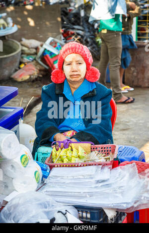 Femme locale exposant portant thanaka et un chapeau en tricot rouge avec pompons au Marché de Jade, Mandalay, Myanmar (Birmanie) Banque D'Images