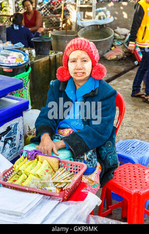 Femme locale exposant portant thanaka et un chapeau en tricot rouge avec pompons au Marché de Jade, Mandalay, Myanmar (Birmanie) Banque D'Images