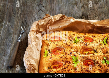 Focaccia italienne fraîchement cuit au four avec des tomates sur une vieille table en bois. Banque D'Images