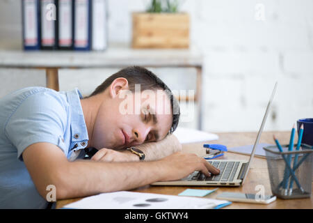 Portrait de jeune homme allongé sur la table en face de l'ordinateur portable, endormi, fatigué, surmené ou paresseux au travail. L'homme d'affaires attrayant Banque D'Images