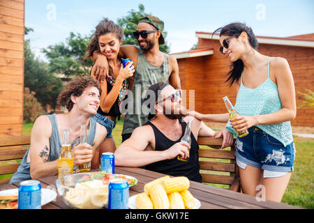 Happy group of teenage friends sitting at table boire de la bière et manger des collations Banque D'Images