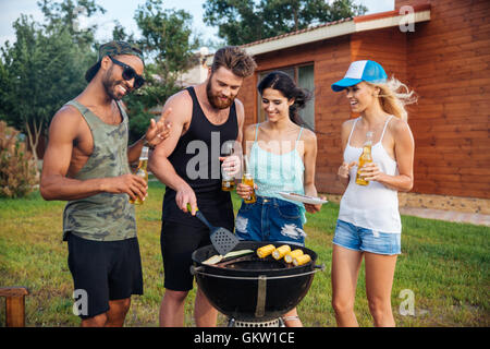 Group of smiling jeunes boire de la bière et de la cuisson sur barbecue grill en plein air Banque D'Images