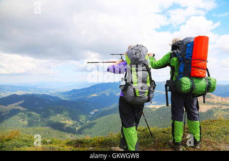 Couple de randonneurs qui montre la voie avec les bâtons de trekking sur le sommet de la montagne Banque D'Images