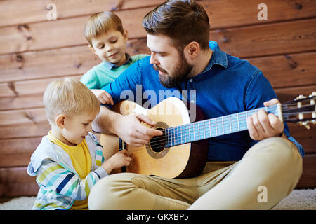Homme barbu playin guitare avec deux fils près de par Banque D'Images