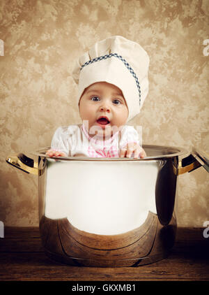 Mignon bébé chef dans un énorme chaudron sur table en bois Banque D'Images