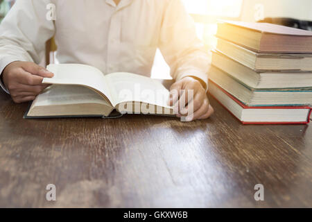 Man reading book avec pile de manuels sur la bibliothèque de bureau en bois Banque D'Images