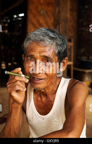 Un homme birman de fumer à sa maison dans Minnathu Village près de Bagan, Myanmar (Birmanie). L'homme fume un cigare roulé à l'échelle locale. Banque D'Images