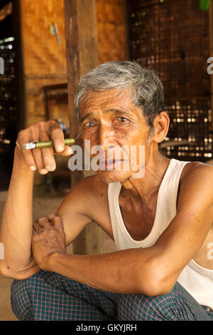 Un homme birman de fumer à sa maison dans Minnathu Village près de Bagan, Myanmar (Birmanie). L'homme fume un cigare roulé à l'échelle locale. Banque D'Images