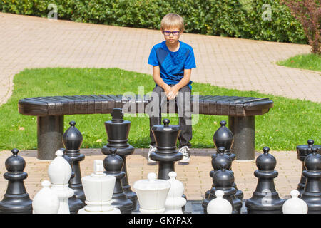 Enfant concentré, à penser à son prochain déplacement, assis sur un banc en bois, au cours d'une partie d'échecs à l'aide de morceaux de vie et conseil Banque D'Images