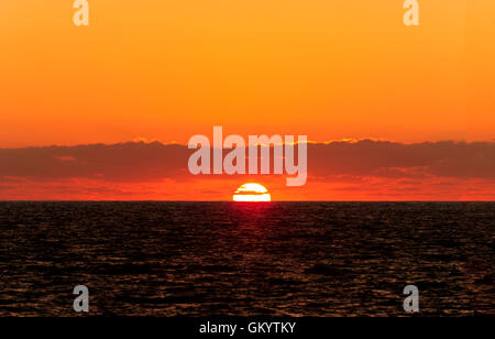 Ocean sunset est un chaud soleil blanc réglage sur l'horizon de l'océan sous une couche de nuages tout au sein d'un superbe ciel coucher de soleil orange. Banque D'Images