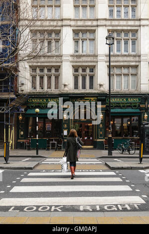 Femme marche sur passage pour piétons sur Charing Cross Road en direction de Garrick Arms pub, Londres. Banque D'Images