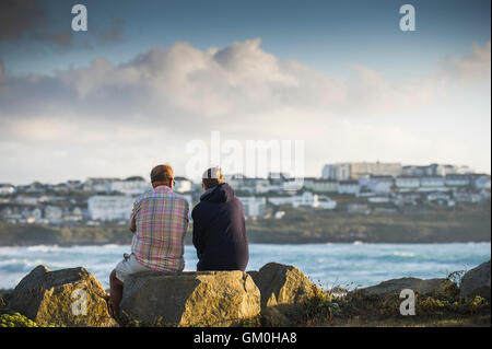 Deux vacanciers, s'asseoir sur des rochers surplombant dans Fistral Newquay, Cornwall. Banque D'Images