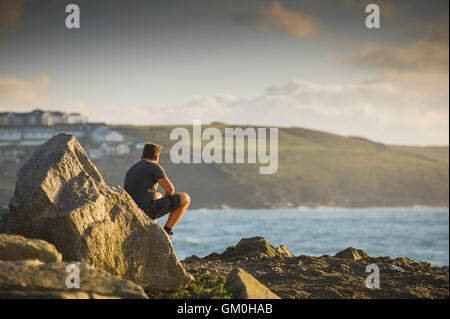 Un homme est assis sur un rocher surplombant la mer à Pointe de Towan à Newquay, Cornwall. Banque D'Images