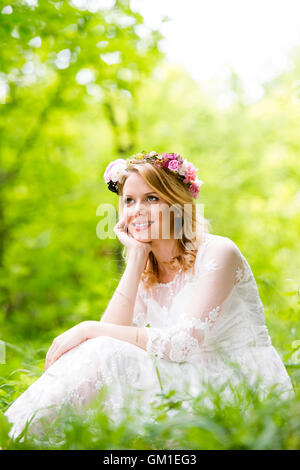 Mariée en robe de mariage avec couronne de fleurs, vert nature. Banque D'Images