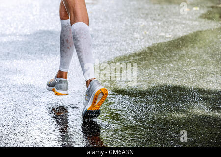 Les jambes des femmes minces dans des chaussettes de compression marathonien, tournant dans une flaque d'eau, des jets d'eau Banque D'Images