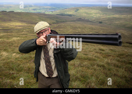 Un homme cherche son fusil pendant une grouse tourner en haute sur le Yorkshire Moors, swinithwaite dans Yorkshire du nord. Banque D'Images