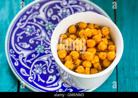 Pois chiches rôtis avec différentes épices dans un bol blanc sur fond bleu Banque D'Images