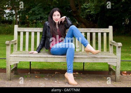 Jeune femme assise sur un banc de parc posing Banque D'Images