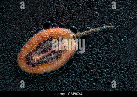 Tamarillo réduit de moitié des fruits dans de l'eau minérale, une série de photos. Close-up de l'eau gazéifiée sur fond noir Banque D'Images