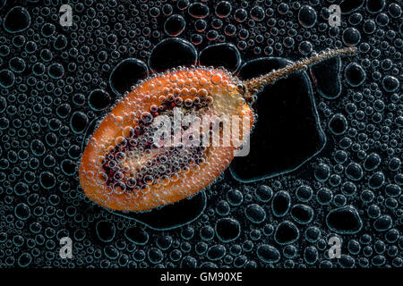 Tamarillo réduit de moitié des fruits dans de l'eau minérale, une série de photos. Close-up de l'eau gazéifiée sur fond noir Banque D'Images