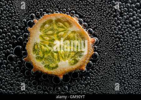 Kiwano fruit melon à cornes, dans l'eau minérale, une série de photos. Close-up de l'eau gazéifiée sur fond noir Banque D'Images