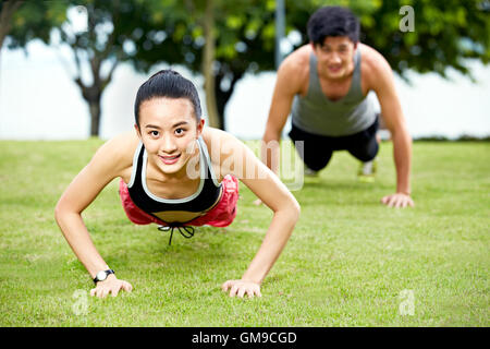 Young Asian man and woman couple doing push-ups de l'herbe dans un parc de la ville. Banque D'Images