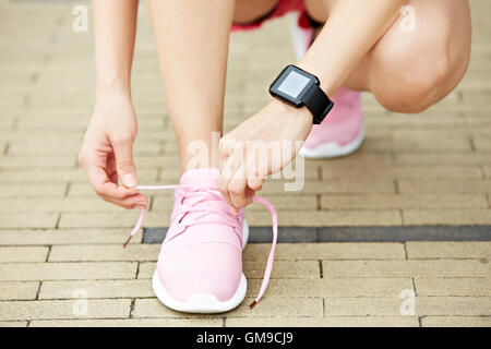 Jeune femme runner avec appareil de fitness portable lacet de liage, close-up. Banque D'Images