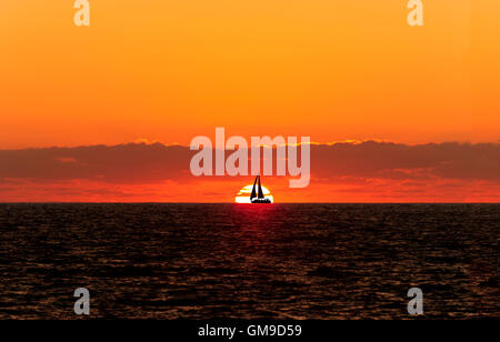 Voilier sunset silhouette est un bateau naviguant en toute voiles dehors silhouetted against a white réglage chaud soleil et orange vif Banque D'Images