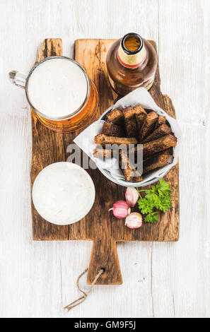 Snack-bière ensemble. Pinte de bière Pilsener dans une tasse, ouvrir le flacon en verre, croûtons de pain de seigle à la crème d'ail de la sauce au fromage sur conseil rustique en bois peint en blanc au fond ancien Banque D'Images