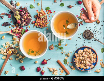 Deux tasses de thé à base de plantes en bonne santé avec la menthe, cannelle, rose, fleurs de camomille séchées dans des cuillères et man's hand holding spoon Banque D'Images