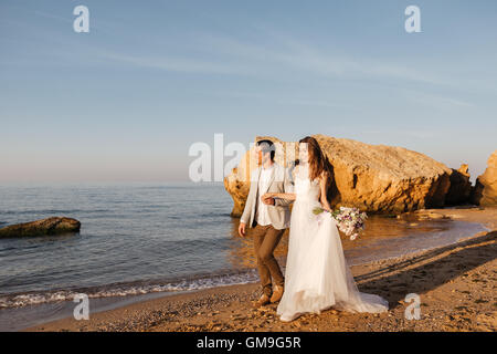 Couple marié juste à marcher à la plage au coucher du soleil Banque D'Images