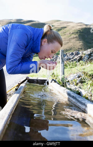 L'Autriche, Salzburger Land, Weissbach, mature woman drinking water de l'ancien abreuvoir en bois Banque D'Images