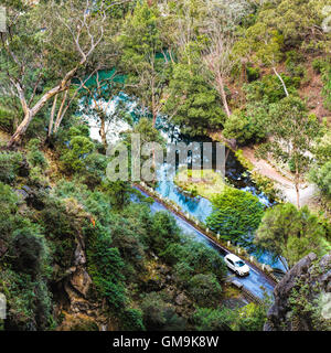 L'Australie, Nouvelle Galles du Sud, des grottes de Jenolan, Blue Lake, Voiture sur route au bord du lac entre les pentes couvertes de forêts Banque D'Images