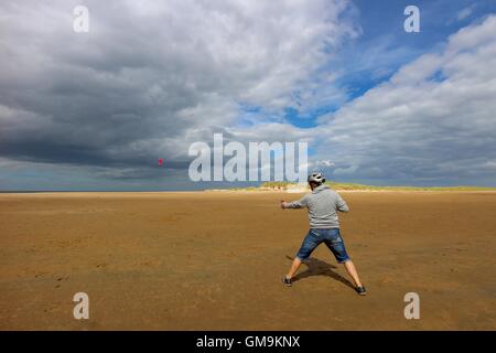 Vue de derrière un homme portant un cerf-volant jeans récolte sur holkham beach North Norfolk par un jour de vent -nuageux ciel bleu orageux Banque D'Images