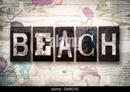 Le mot 'Beach' écrit en vintage metal sale type typographique sur un fond de bois blanchis par l'encre et de taches de peinture. Banque D'Images