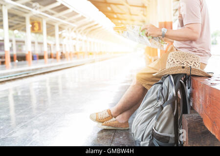 Jeune homme tenant une carte avec sac à dos, assis sur la plate-forme à la gare - travel concept Banque D'Images