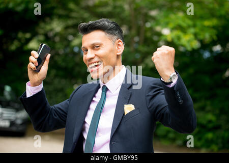 Homme d'affaires joyeuse à peau d'olive avec bras levés et tenant le téléphone mobile dans une main. Banque D'Images