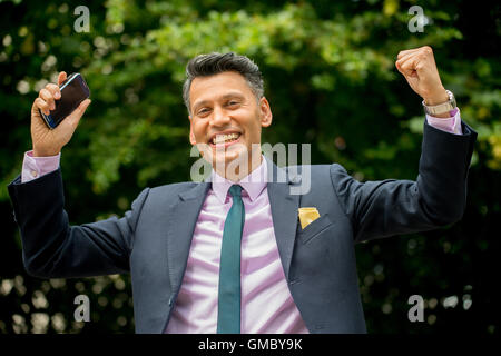 Homme d'affaires joyeuse à peau d'olive avec bras levés et tenant le téléphone mobile dans une main. Banque D'Images