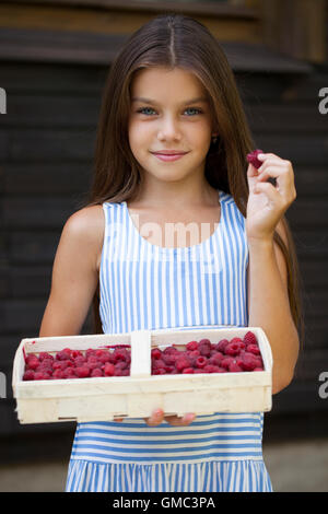 Belle brune petite fille tenant une boîte avec une framboise, été dehors Banque D'Images