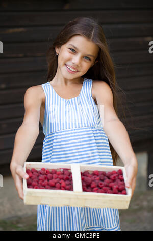 Belle brune petite fille tenant une boîte avec une framboise, été dehors Banque D'Images