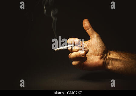 Composition conceptuelle sur le tabagisme, studio shot de la main d'un homme tenant un cigare. Banque D'Images