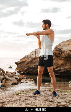 Beau jeune homme sportif étend les mains avant de courir à la plage Banque D'Images