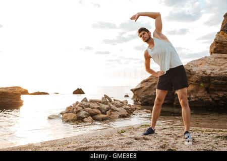 Beau jeune homme sportif doing stretching avant de courir à la plage Banque D'Images