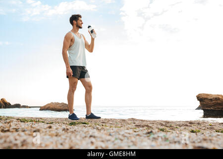Jeune homme sportif sportif se reposant après le jogging sur la plage et l'eau potable Banque D'Images