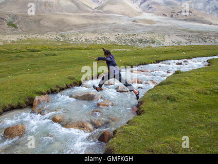 Wakhi garçon sautant par-dessus une rivière de pamir, Grand pamir, Afghanistan, Wakhan Banque D'Images